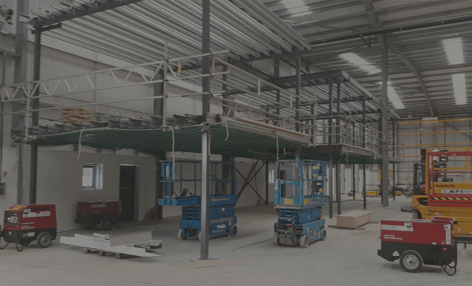 Mezzanine floor steelwork under construction in a warehouse, with scissor lifts on site